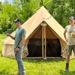 Group of campers standing outside a spacious 8-person canvas bell tent in a grassy campsite surrounded by trees.