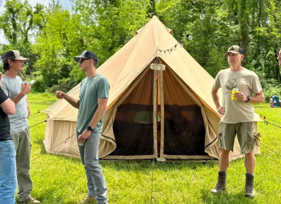 Group of campers standing outside a spacious 8-person canvas bell tent in a grassy campsite surrounded by trees.