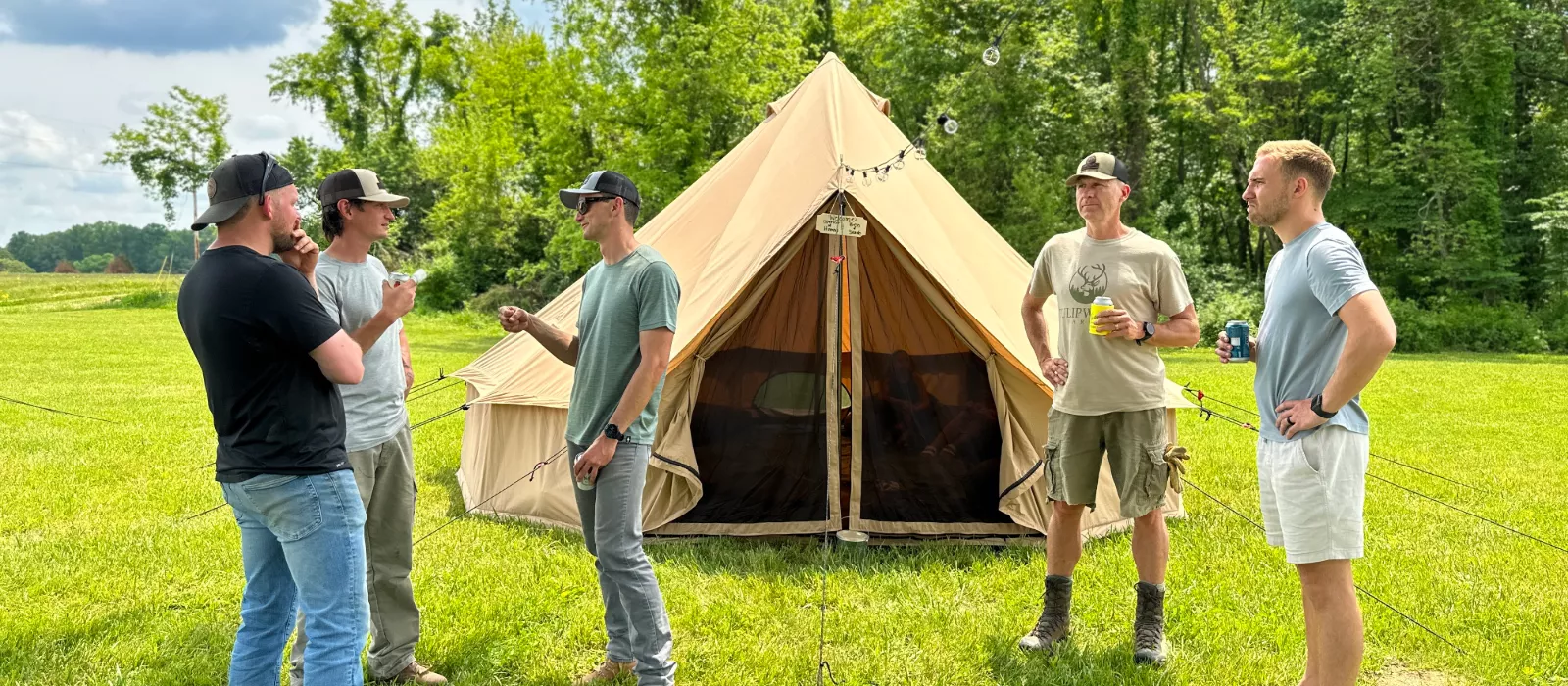 Group of campers standing outside a spacious 8-person canvas bell tent in a grassy campsite surrounded by trees.
