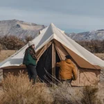 Two campers setting up a canvas bell tent in a dry mountain landscape during winter camping.