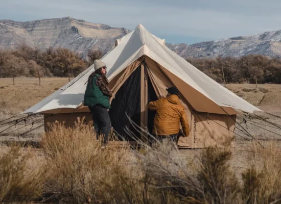 Campers setting up a canvas bell tent in a scenic mountain landscape during outdoor camping trip.
