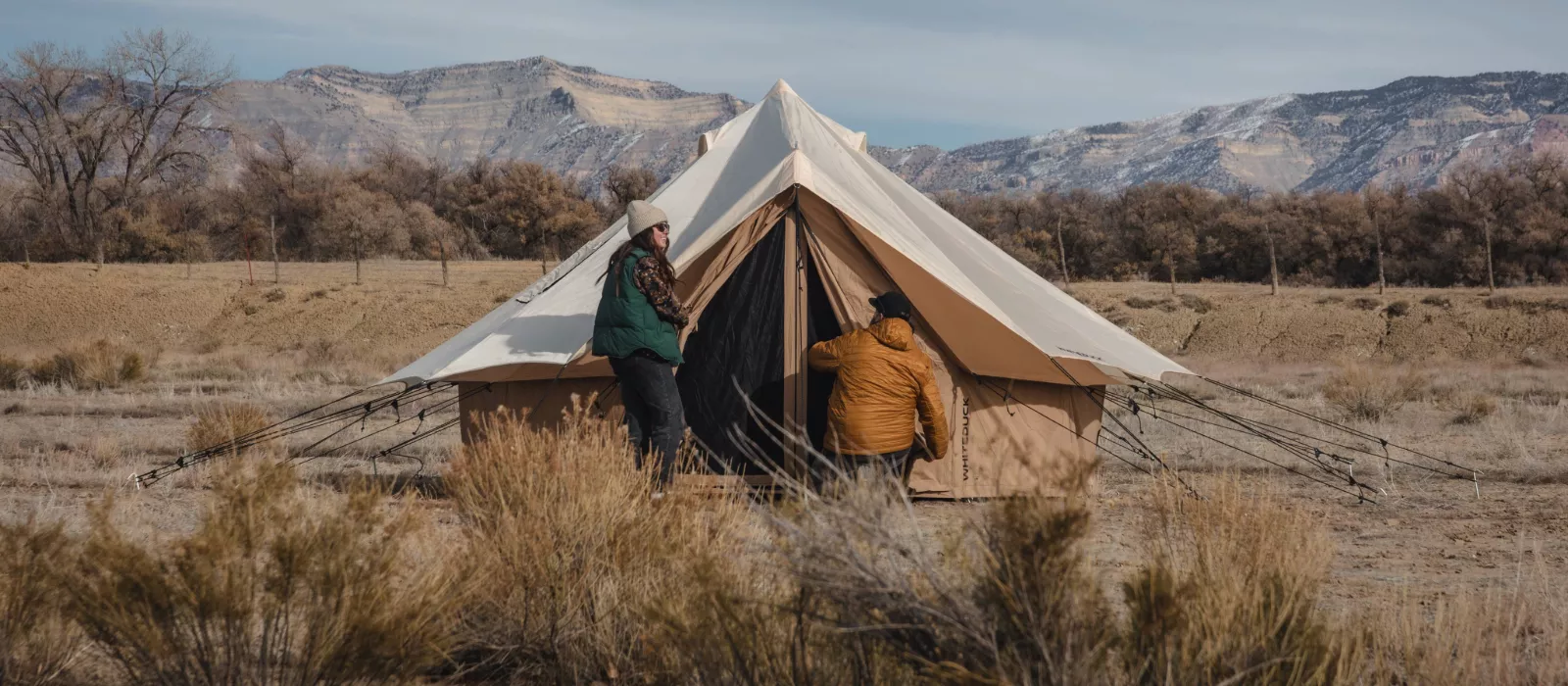 Campers setting up a canvas bell tent in a scenic mountain landscape during outdoor camping trip.