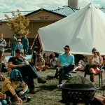 Optimus Avalon canvas tent displayed at an outdoor event with people gathered around the seating area and fire pit.