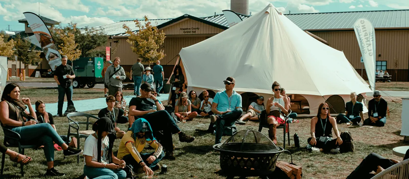 Optimus Avalon canvas tent displayed at an outdoor event with people gathered around the seating area and fire pit.