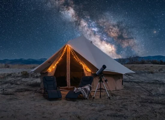 Luxury glamping tent in a desert landscape under the Milky Way galaxy with telescope and outdoor chairs at night.