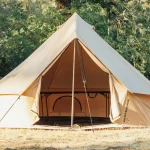 White Duck bell canvas tent set up at a forest campsite with open front entrance and guy lines secured outdoors.