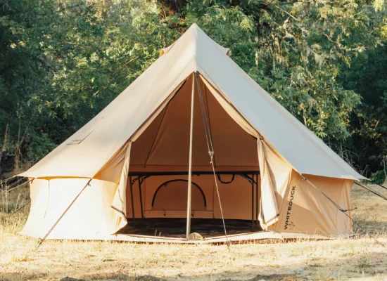 White Duck bell canvas tent set up at a forest campsite with open front entrance and guy lines secured outdoors.