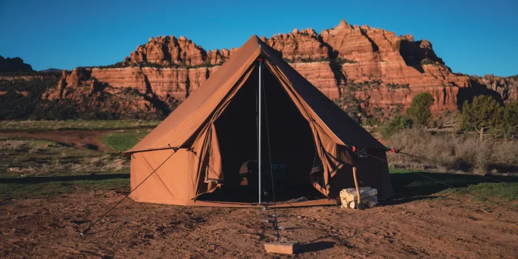 Brown canvas bell tent set up on a desert campsite with red rock mountains and clear blue sky in the background.