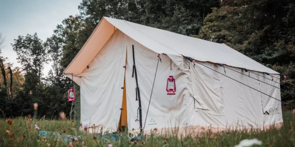 Large white canvas wall tent pitched in a grassy meadow surrounded by trees, with lanterns hanging outside.