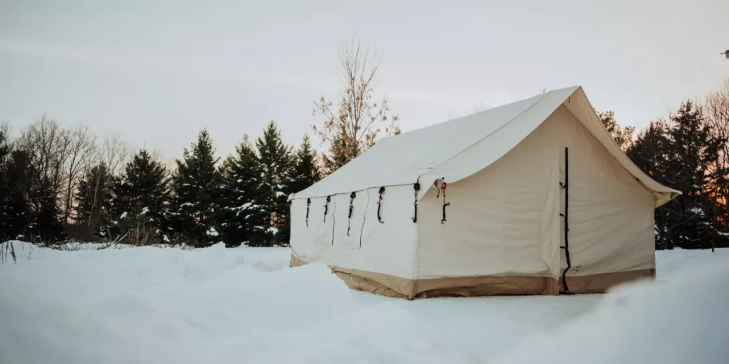 Canvas wall tent set up in a snow-covered landscape surrounded by evergreen trees, showcasing a four-season camping shelter for winter adventures.