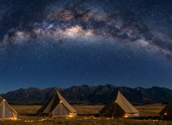 Canvas bell tents illuminated at night beneath the Milky Way galaxy, set against a mountain backdrop in a remote camping destination.