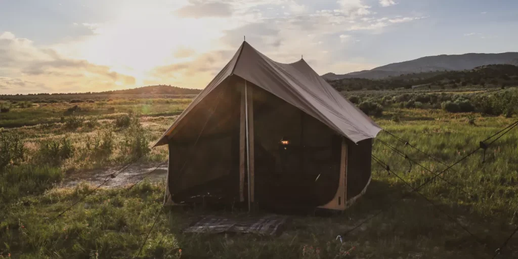 Rover Scout Tent set up in a grassy meadow at sunrise, featuring a durable canvas design with mountain views in the background.