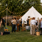 Backyard micro wedding with guests gathered around a white bell tent and string lights