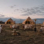 Outdoor wedding event with canvas bell tents, string lights, dining tables, and mountain views