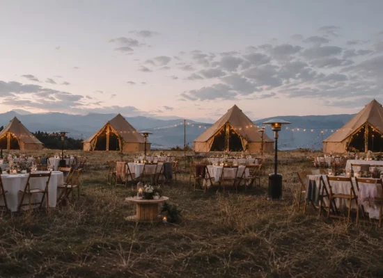 Outdoor wedding event with canvas bell tents, string lights, dining tables, and mountain views