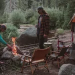 Scout troop gathered around a campfire with a canvas tent set up in a forest campsite