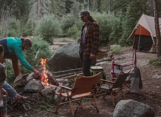 Scout troop gathered around a campfire with a canvas tent set up in a forest campsite