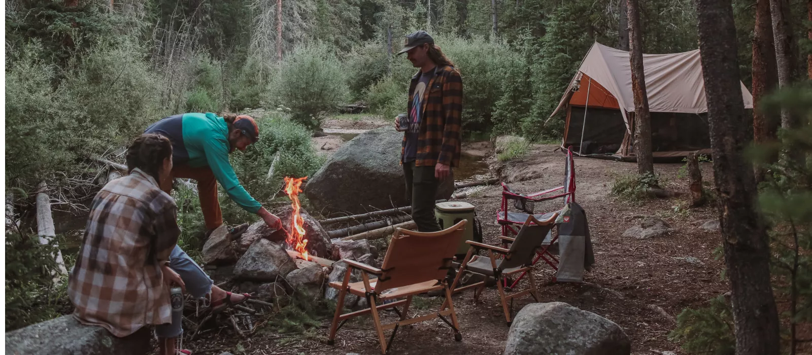 Scout troop gathered around a campfire with a canvas tent set up in a forest campsite
