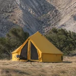 Canvas bell tent standing firm in high winds on a rocky mountain campsite with windswept trees and grass