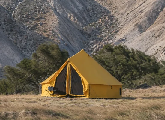 Canvas bell tent standing firm in high winds on a rocky mountain campsite with windswept trees and grass