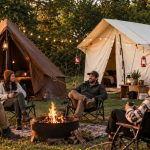 Friends enjoying a cozy glamping trip around a campfire with canvas tents and string lights