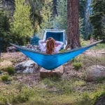 Jess relaxing in a blue hammock at a forest campsite