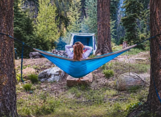 Jess relaxing in a blue hammock at a forest campsite