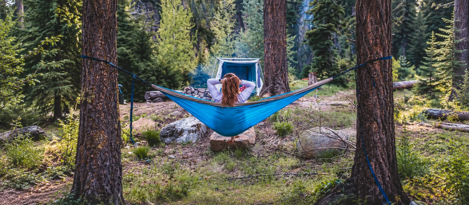 Jess relaxing in a blue hammock at a forest campsite