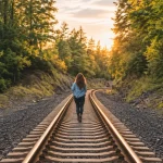Jess walking alone along railroad tracks through a peaceful forest