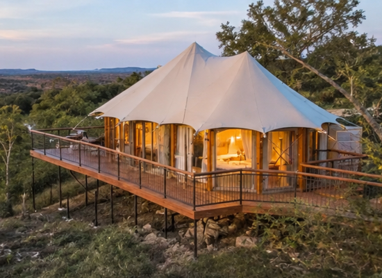 Luxury glamping tent on an elevated wooden deck overlooking the Texas Hill Country at sunset