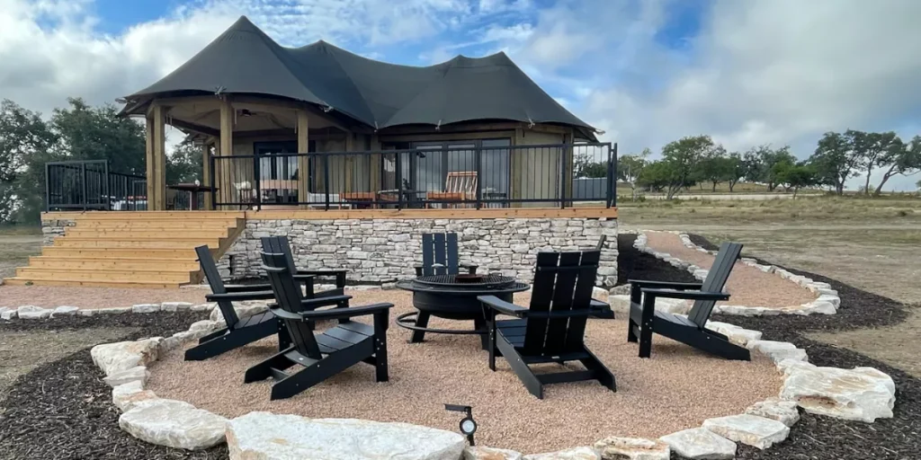 Luxury glamping tent on a raised stone deck with Adirondack chairs and a fire pit overlooking the countryside. Credit: Outdoorsy Hill Country GMB