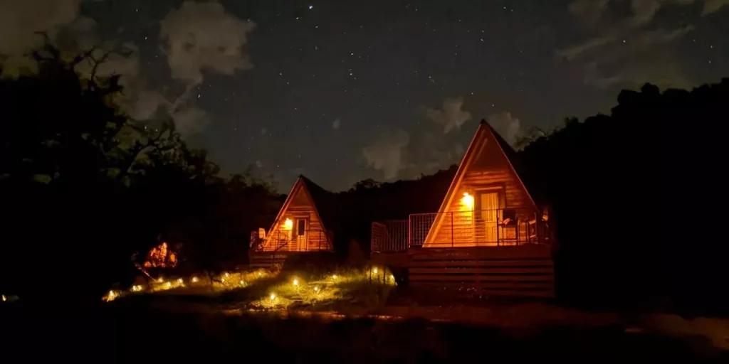 Glamping cabins illuminated at night under a starry sky in a forest setting. Credit: Charmadillo GMB
