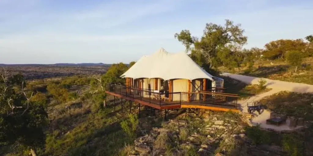 Elevated luxury glamping tent with a wraparound deck overlooking a rugged scenic landscape. Credit: Walden Retreats GMB